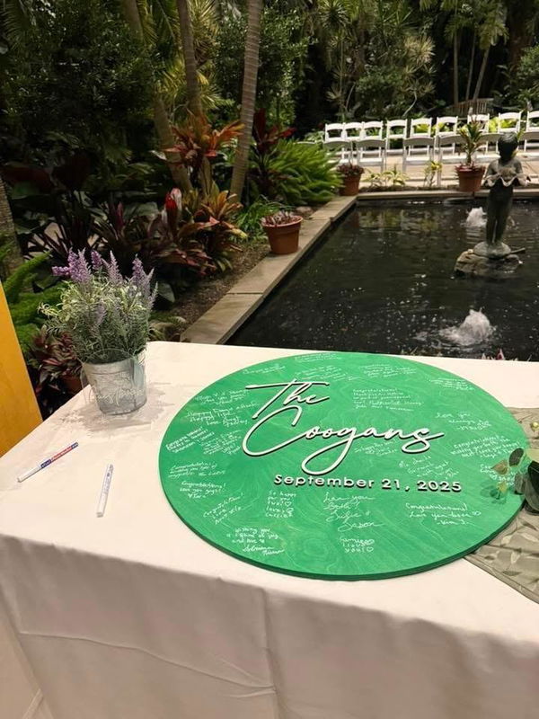 Customer photo: a green round wooden guest book sign covered in guest signatures on a table at an outdoor wedding