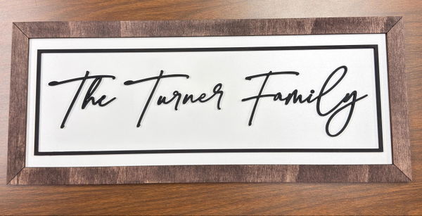 Customer photo: a framed sign reading The Turner Family in black script on a white backer, lying on a wooden desk.