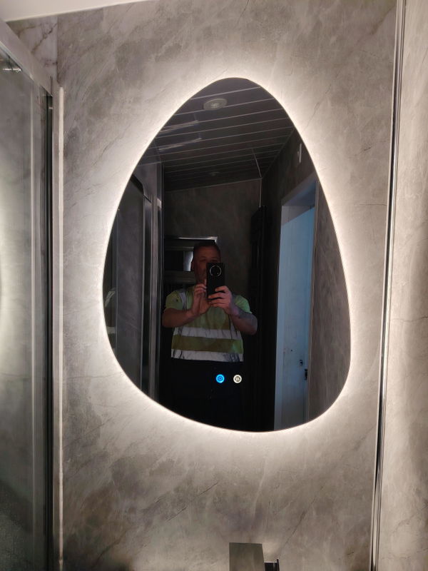 Customer photo of an irregular backlit mirror mounted on a tiled bathroom wall