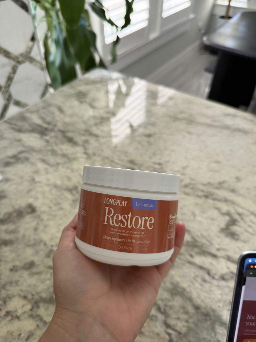 Customer holding a jar of Longplay Restore L-Glutamine powder on a kitchen counter