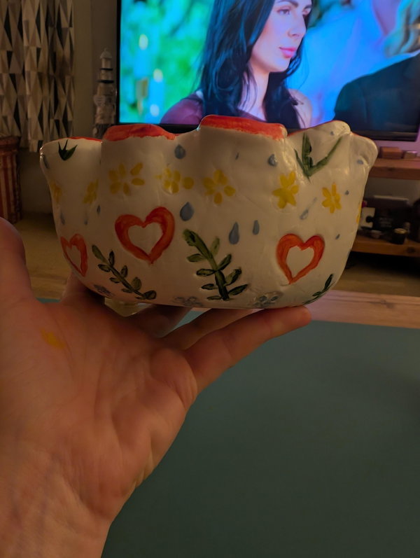 A hand holding a heart patterned clay dish