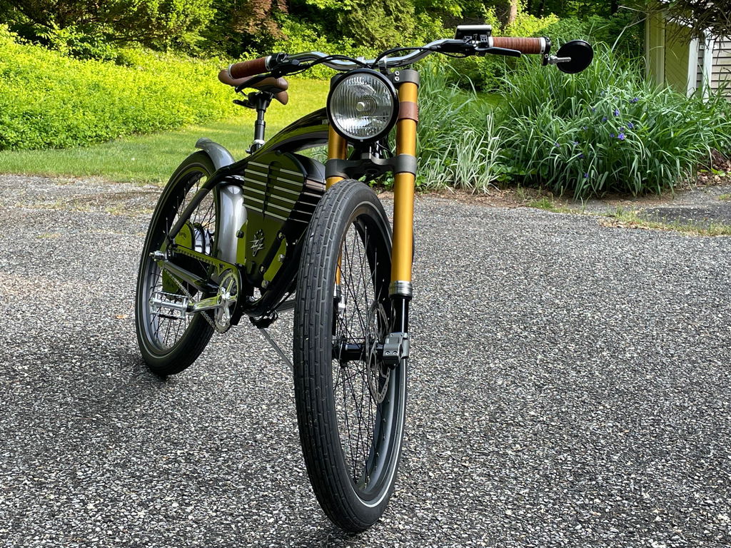 Vintage Roadster with gold front suspension parked beside a garden.
